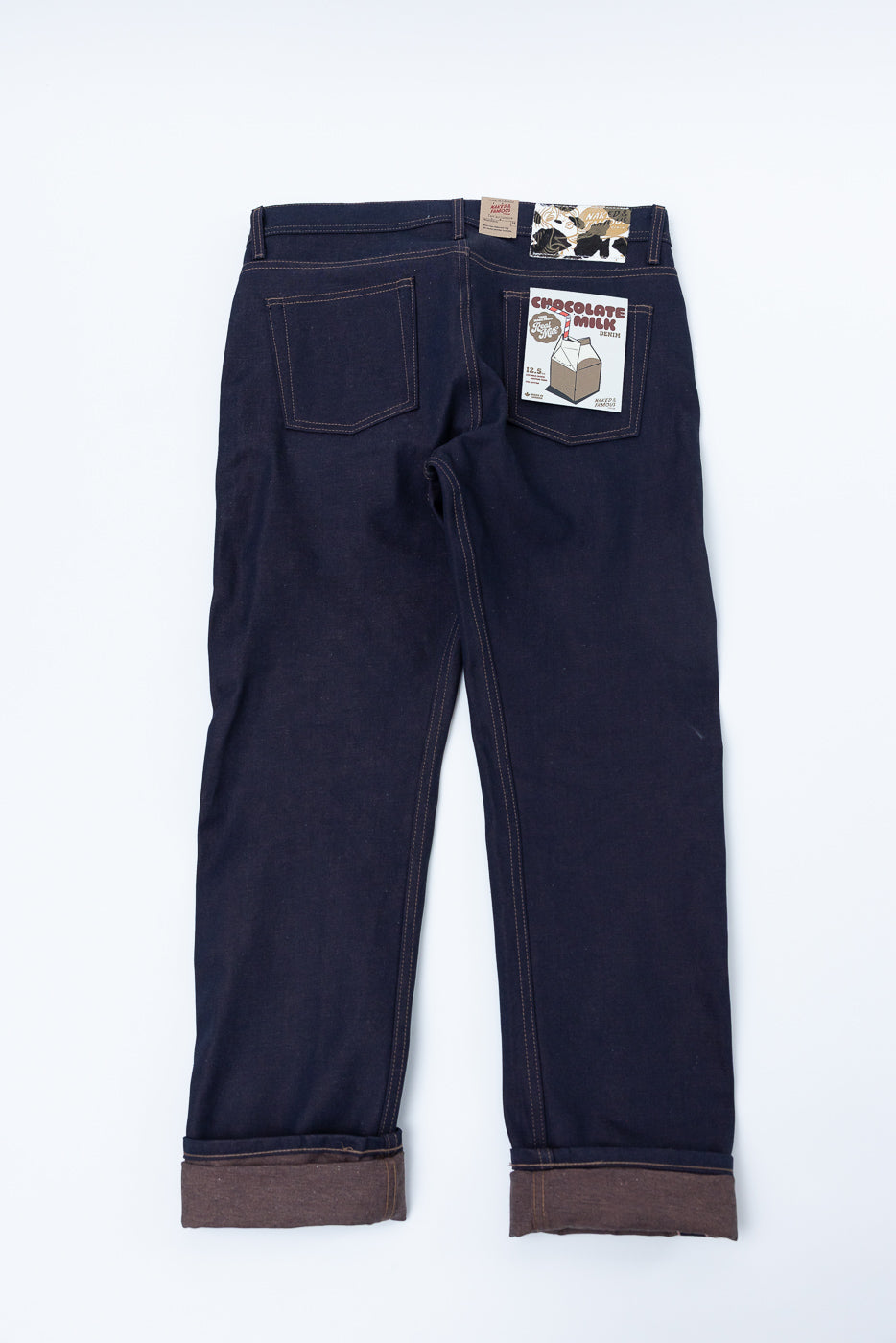 Flat lay of men's raw selvedge denim jeans, back view, showing pockets and turned-up cuffs.