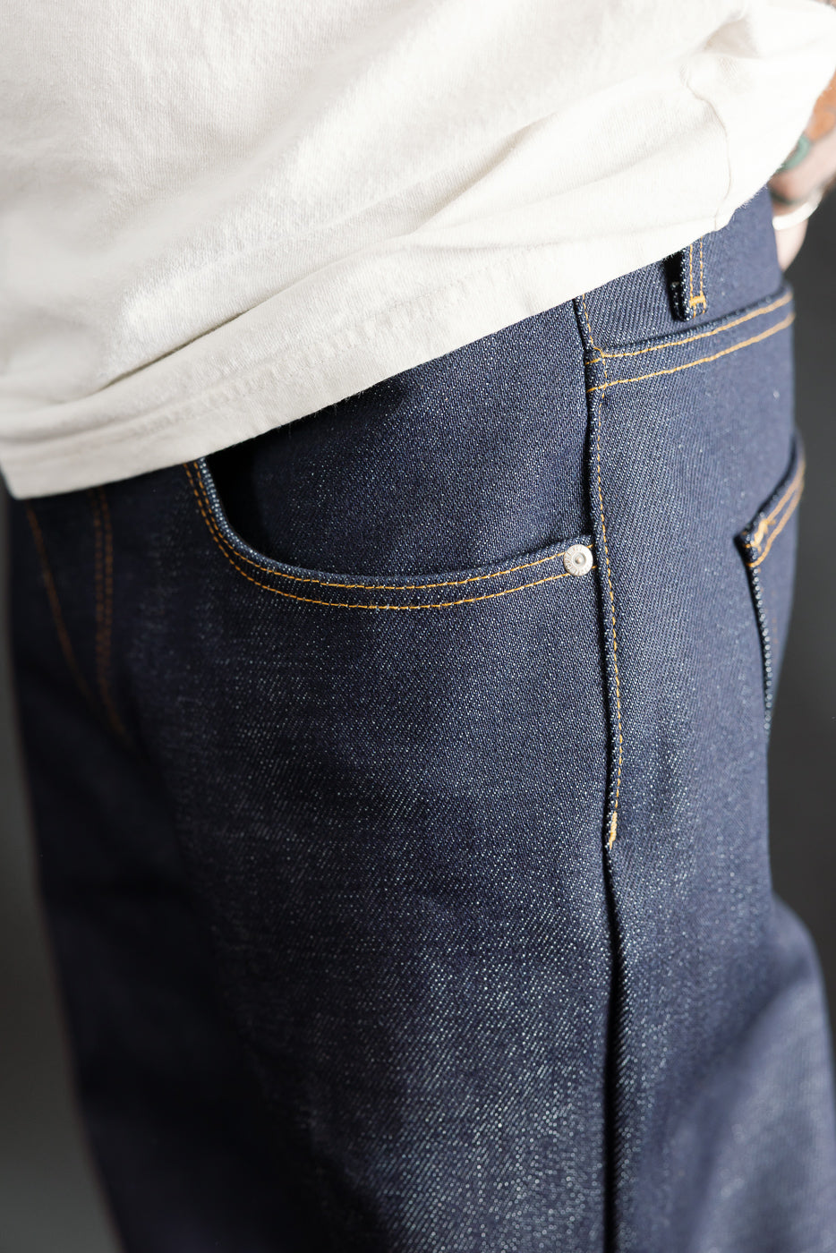 Close-up of front left side of men's Naked & Famous Dirty Elephant 14oz selvedge jeans, showcasing pocket details and raw denim texture. Male model, 5'9