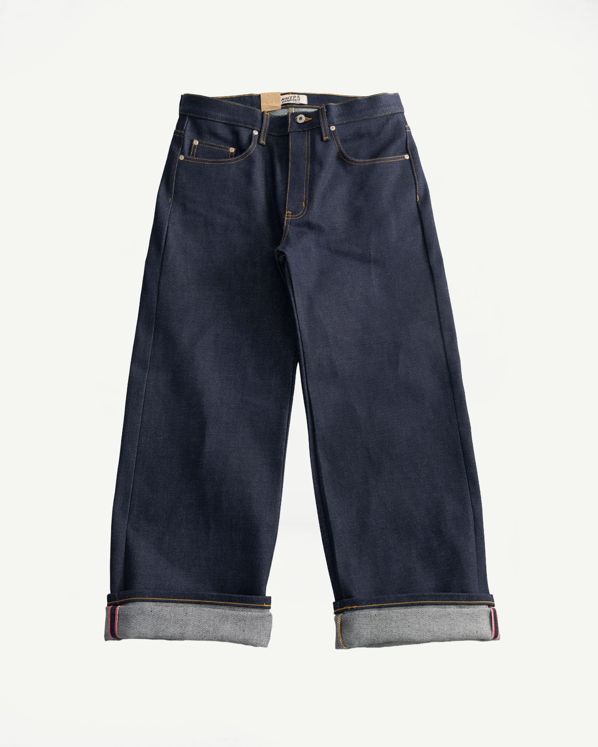 Front flat lay of Naked & Famous Dirty Elephant 14oz Selvedge Strong Guy jeans, dark indigo, visible cuff, gold stitching.