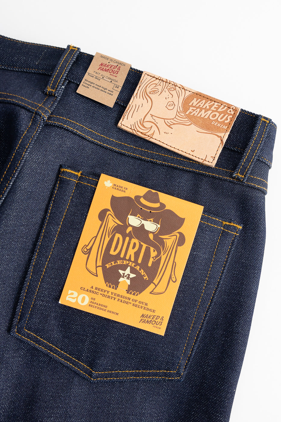 Close-up of Naked & Famous Dirty Elephant 14oz selvedge jeans, back side, showing rear pocket, leather logo patch, and tag details.