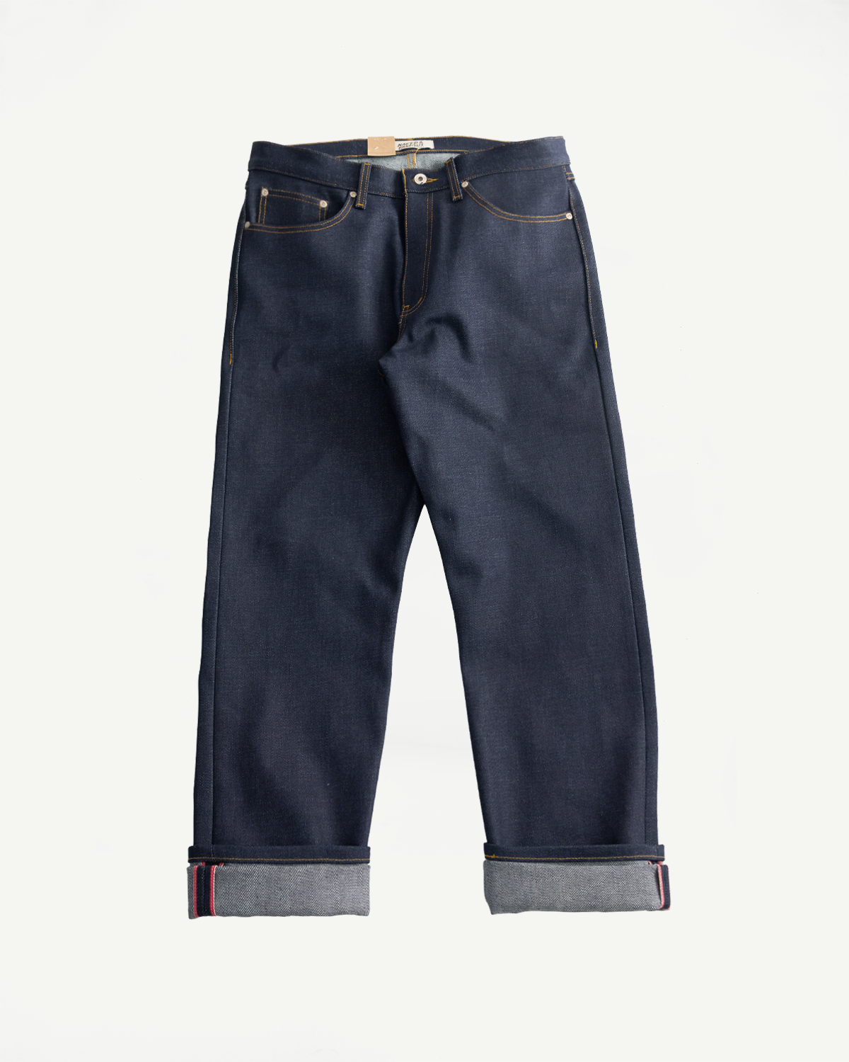 Flat lay front view of Naked & Famous Dirty Elephant selvedge jeans, cuffed, showing front pockets and button fly.