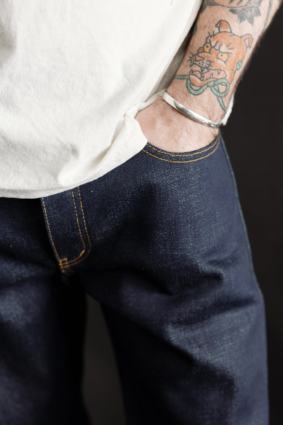 Close-up front view of men's selvedge denim jeans pocket, gold stitching detail, model 5'9