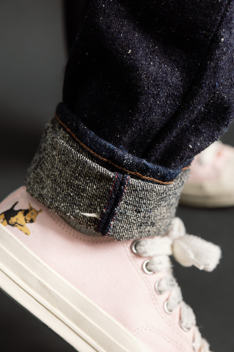 Close-up detail of selvedge denim cuff with visible stitching, worn by male model, leg view