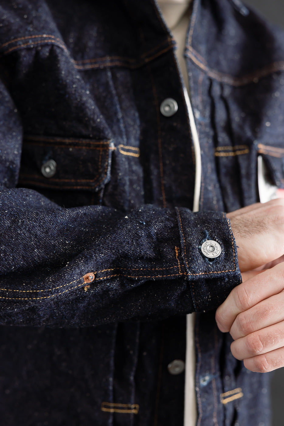 Close-up of men's selvedge denim jacket cuff, chest pocket, and button details, model is male, 5'9