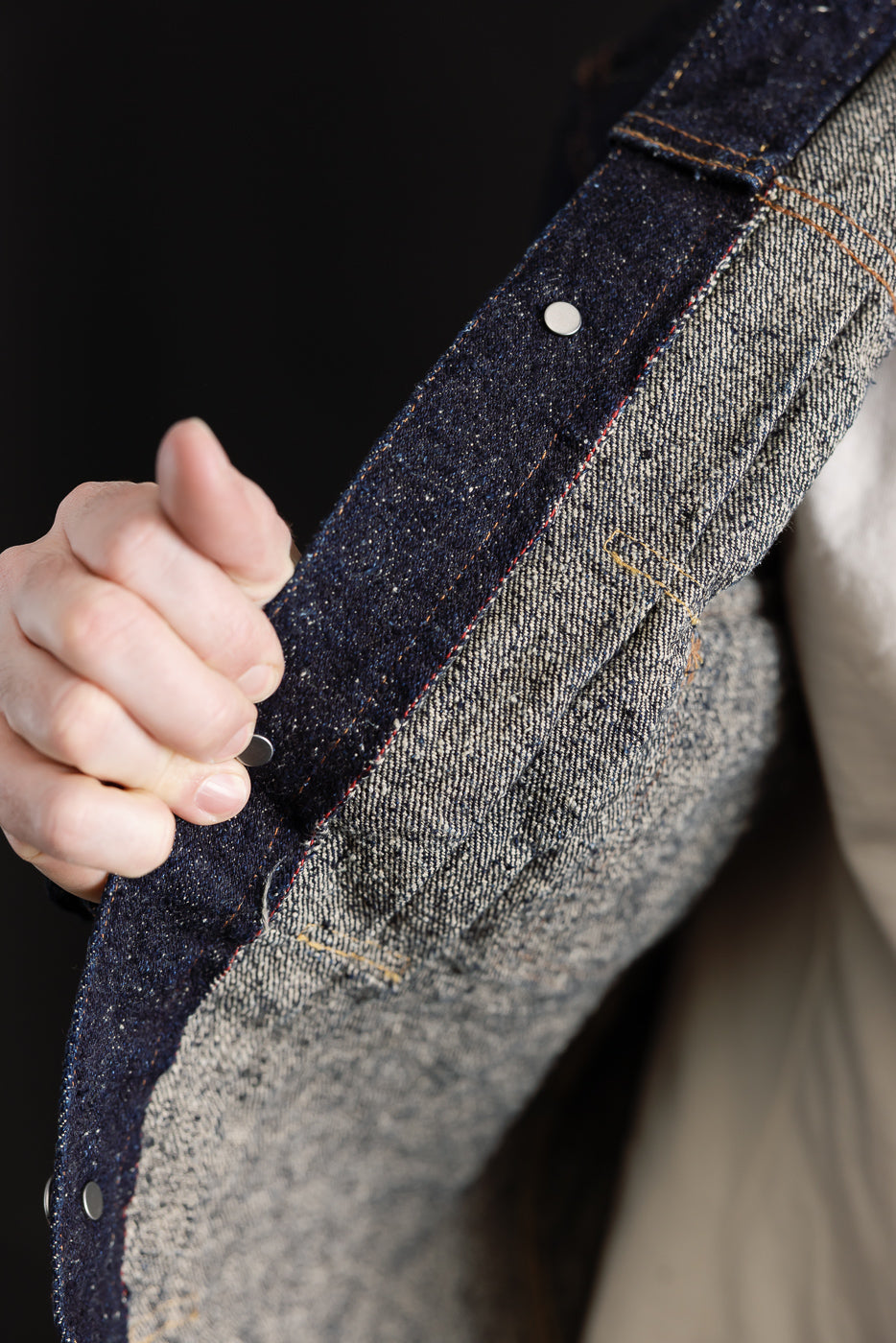 Close-up inside view of Naked & Famous Genseki Selvedge denim jacket front placket, showing fabric texture, contrast stitching, and selvedge ID, modeled by male, 5'9