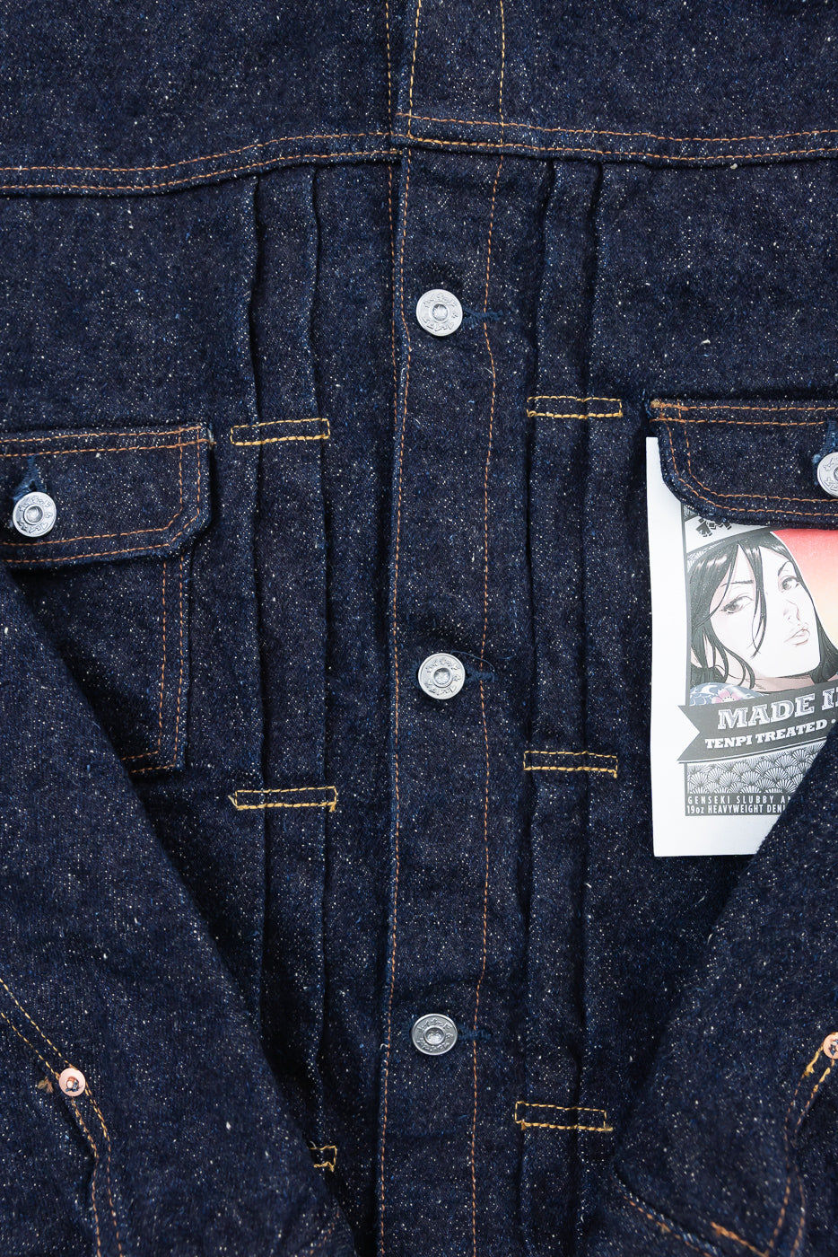 Close-up of front chest and buttons on Naked & Famous Genseki selvedge denim jacket, showing textured indigo fabric, contrast stitching, and pocket details.