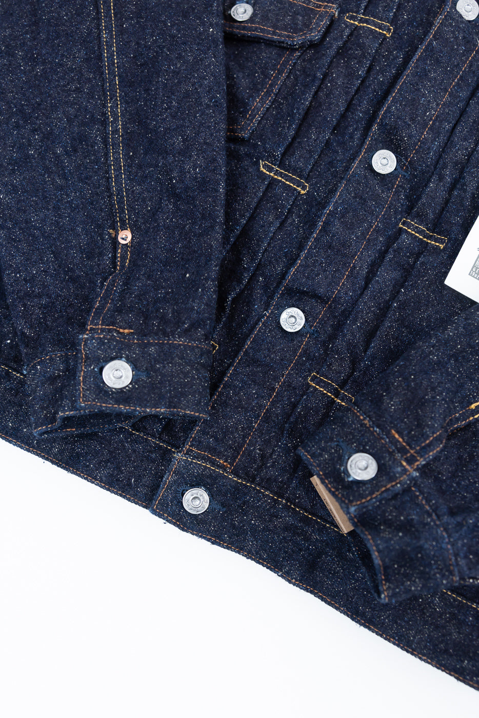 Close-up of Naked & Famous Genseki selvedge denim jacket front, showing cuff, buttons, and textured indigo fabric