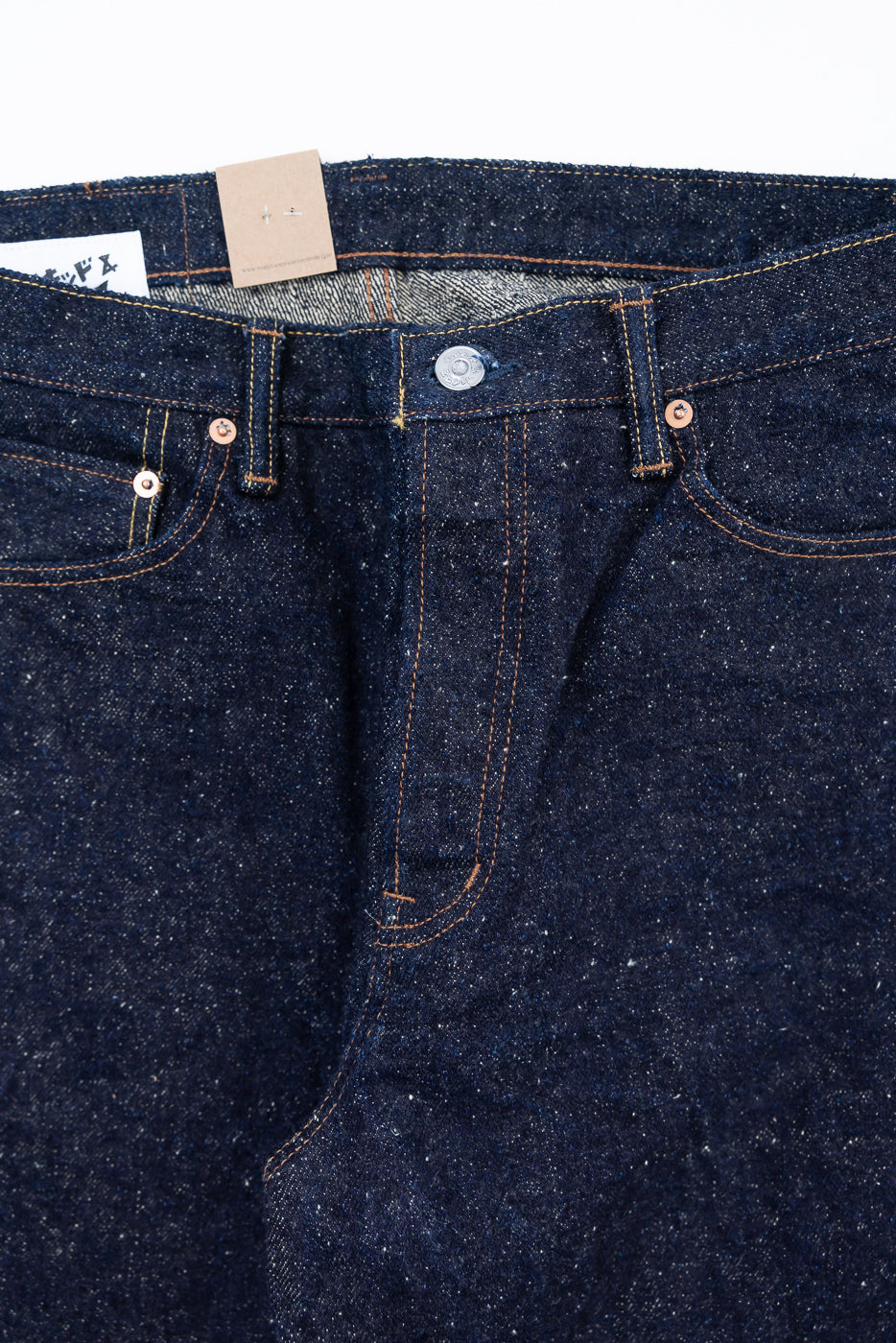 Close-up of front waist and fly of Naked & Famous Genseki Selvedge jeans, highlighting button, rivets, and textured raw denim.