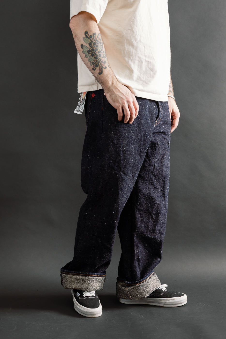 Male model 5'9 165lbs athletic build wearing Naked & Famous Genseki selvedge jeans, side view, showing denim fabric texture and wide cuff, casual styling at Dant