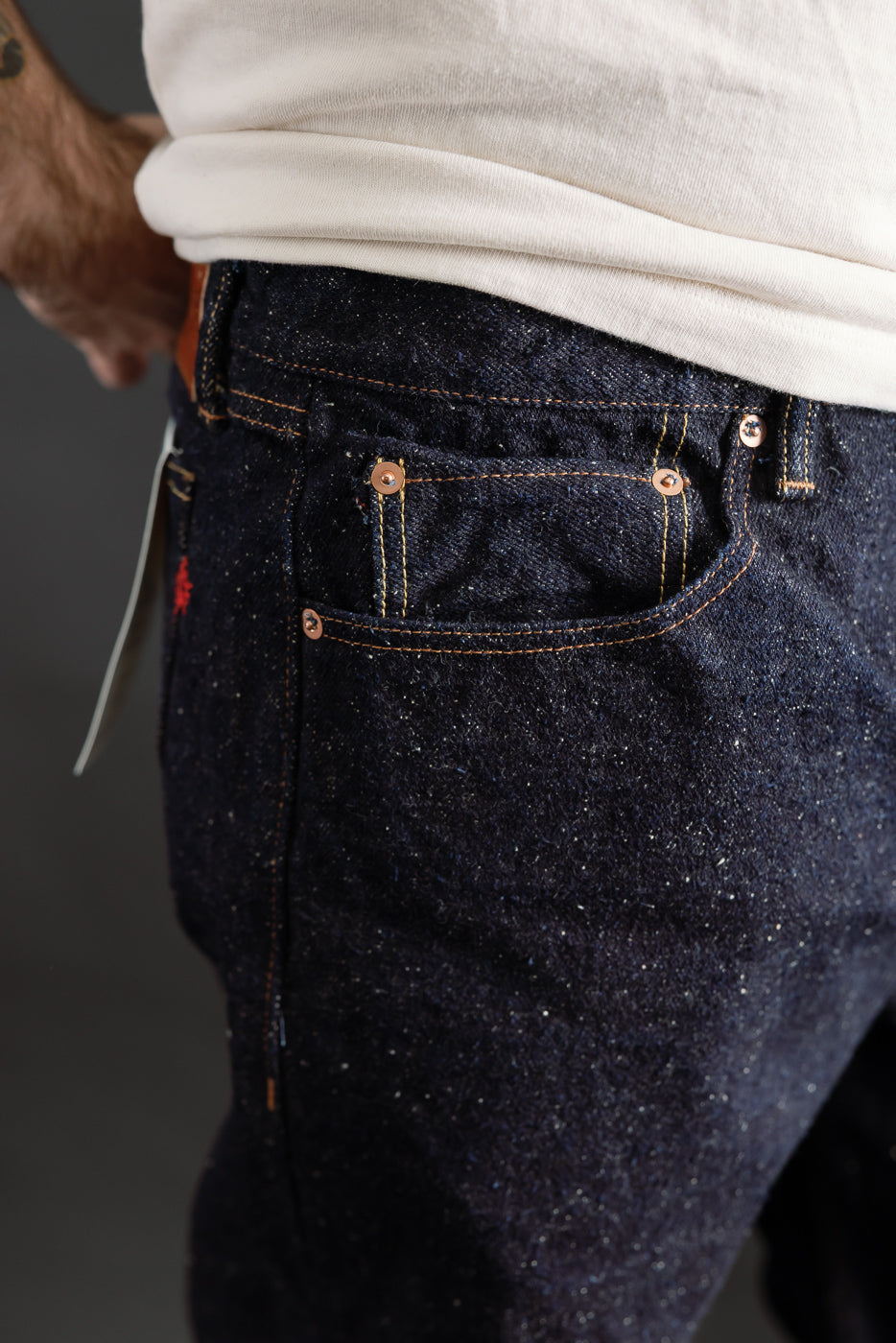 Close-up of front right pocket and upper thigh of Naked & Famous Genseki selvedge jeans on male model, athletic build, showcasing denim texture and copper rivet details.