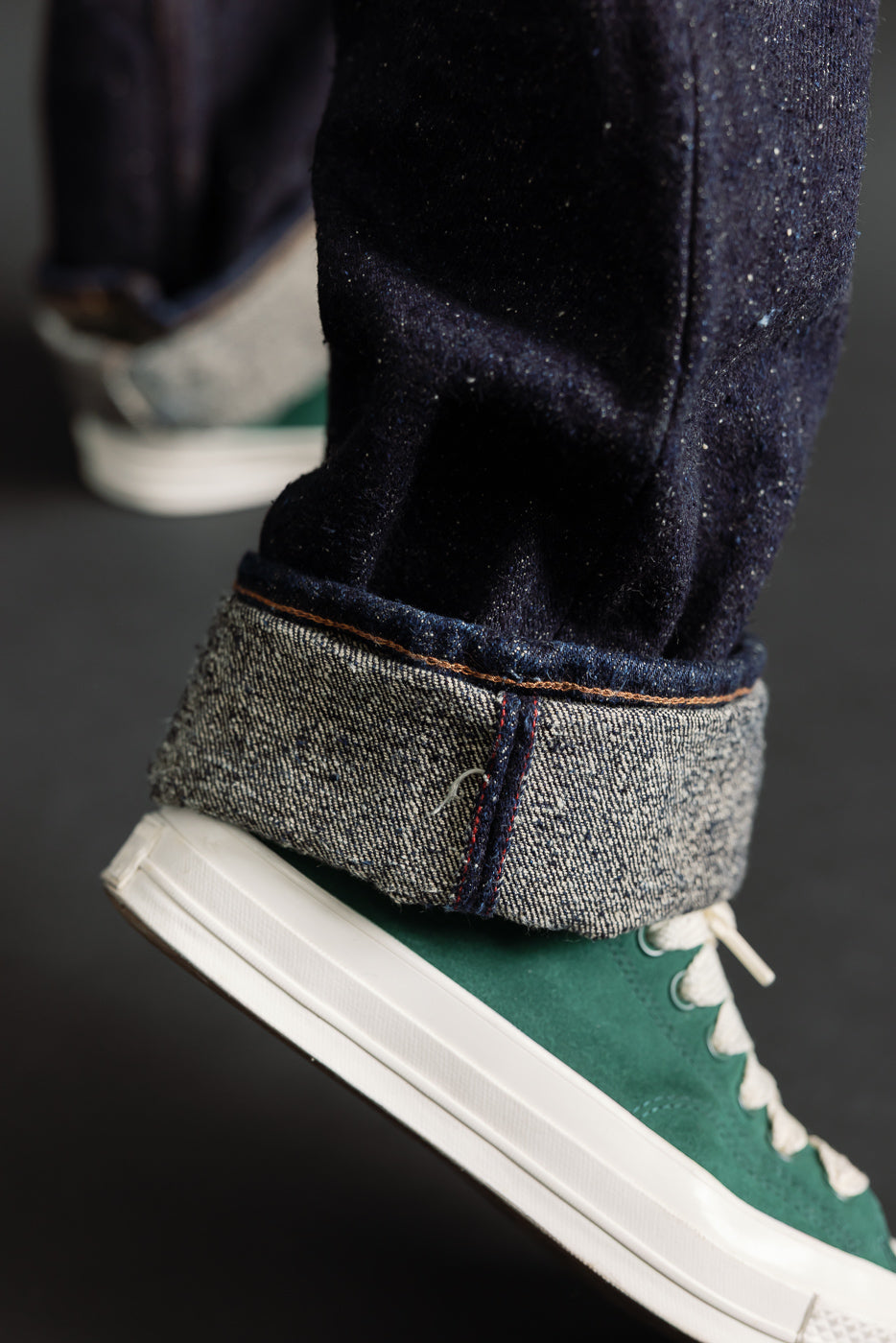 Close-up of male model's cuffed selvedge denim jeans hem and green sneaker, side view