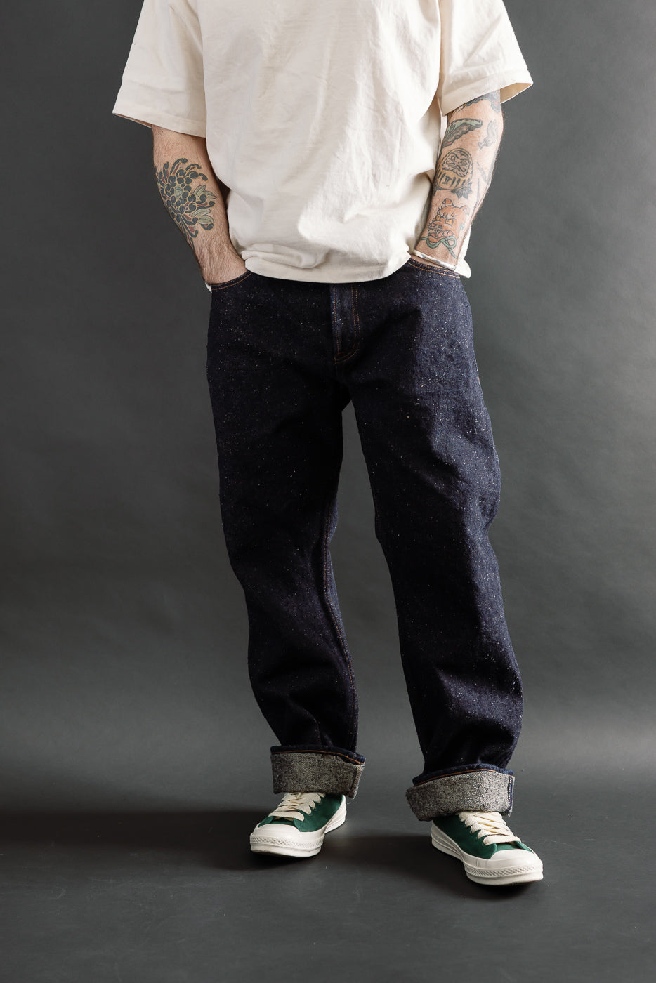 Front view, full body shot of male model 5'9, 165lbs with athletic build wearing Naked & Famous Genseki Selvedge jeans, cuffed, paired with casual white tee and green sneakers at Dant.