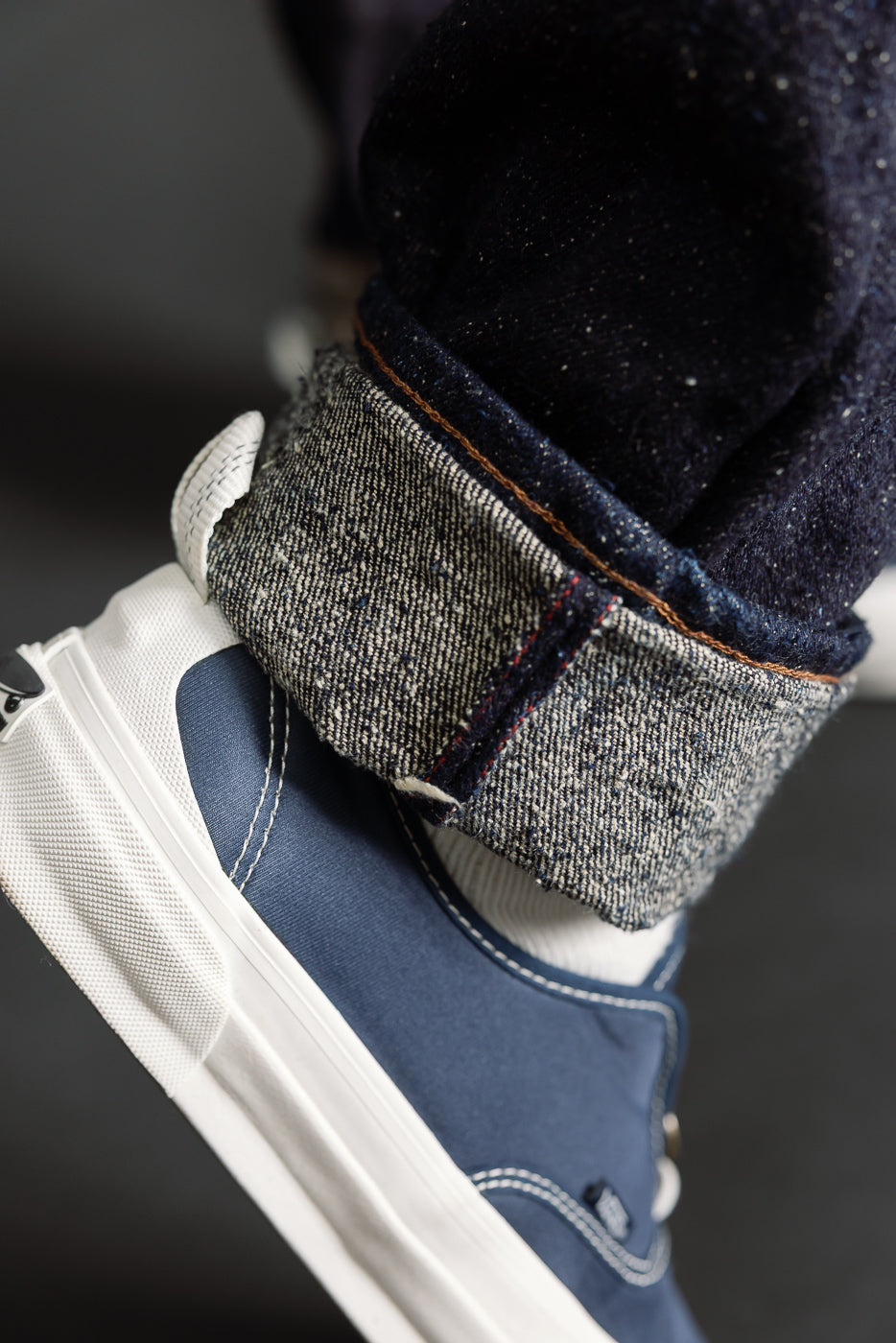 Close-up of men's selvedge denim cuff, showing fabric texture and stitching above sneaker.
