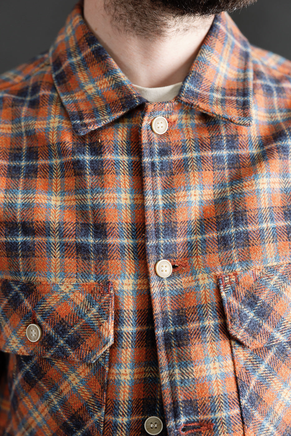 Close-up front view of Naked & Famous triple twist yarn red plaid work shirt on male model, showing button details, chest pockets, and textured fabric, model is 5'9