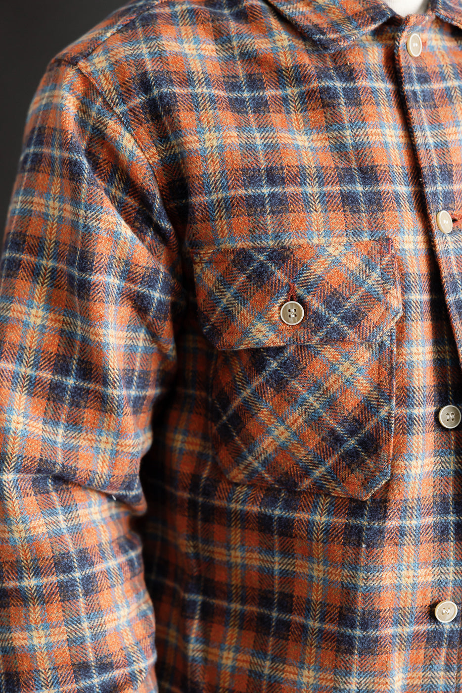 Close-up of men's Naked & Famous work shirt in red triple twist yarn, showing front chest pocket, plaid pattern, textured fabric, and button detail.