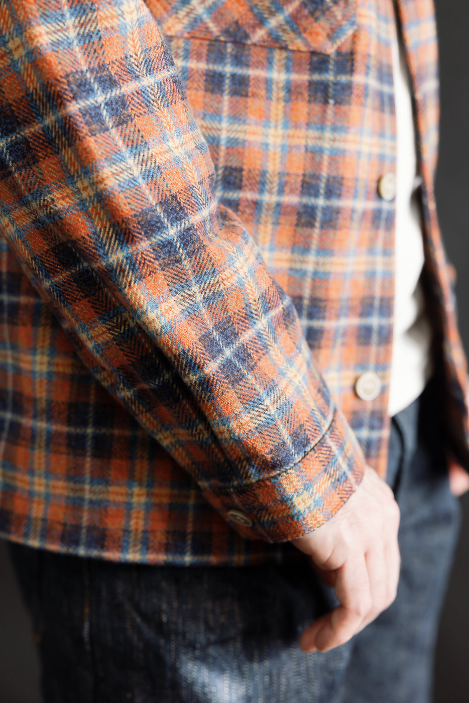 Close-up of male model's right sleeve and front side wearing red plaid work shirt, showing fabric texture and button cuff detail.