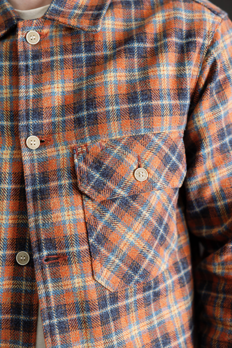 Close-up of front chest area of men's orange and navy plaid work shirt, showing buttoned pocket, collar, and soft textured triple twist yarn fabric at Dant apparel.