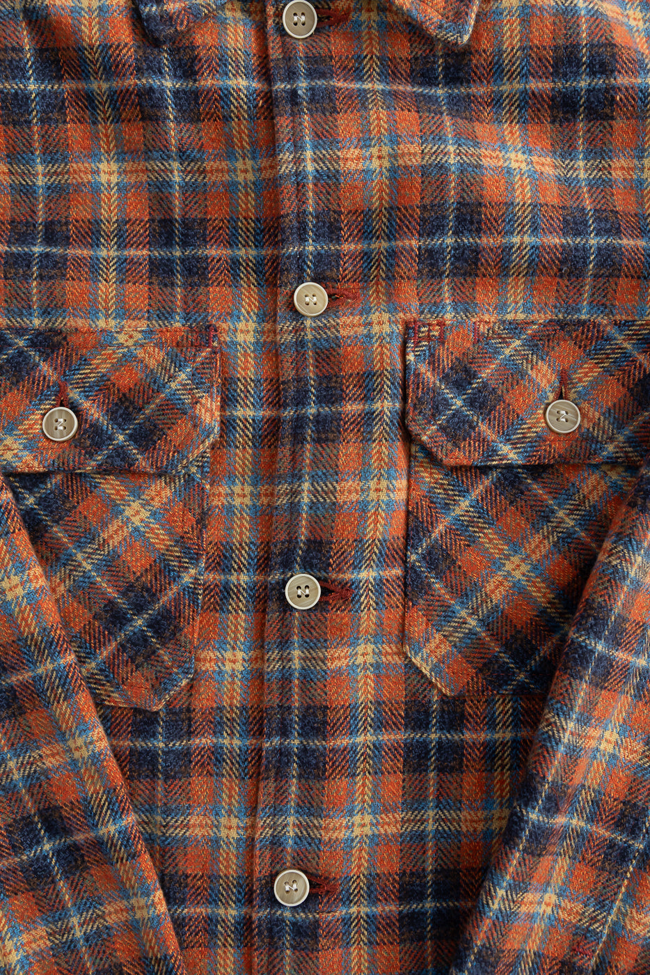 Close-up of front chest on Naked & Famous red plaid work shirt, showing fabric texture, buttons, flap pockets, and collar.