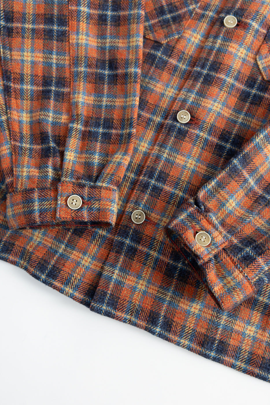 Close-up of Naked & Famous work shirt in red plaid triple twist fabric showing front hem, sleeve cuffs, and button details
