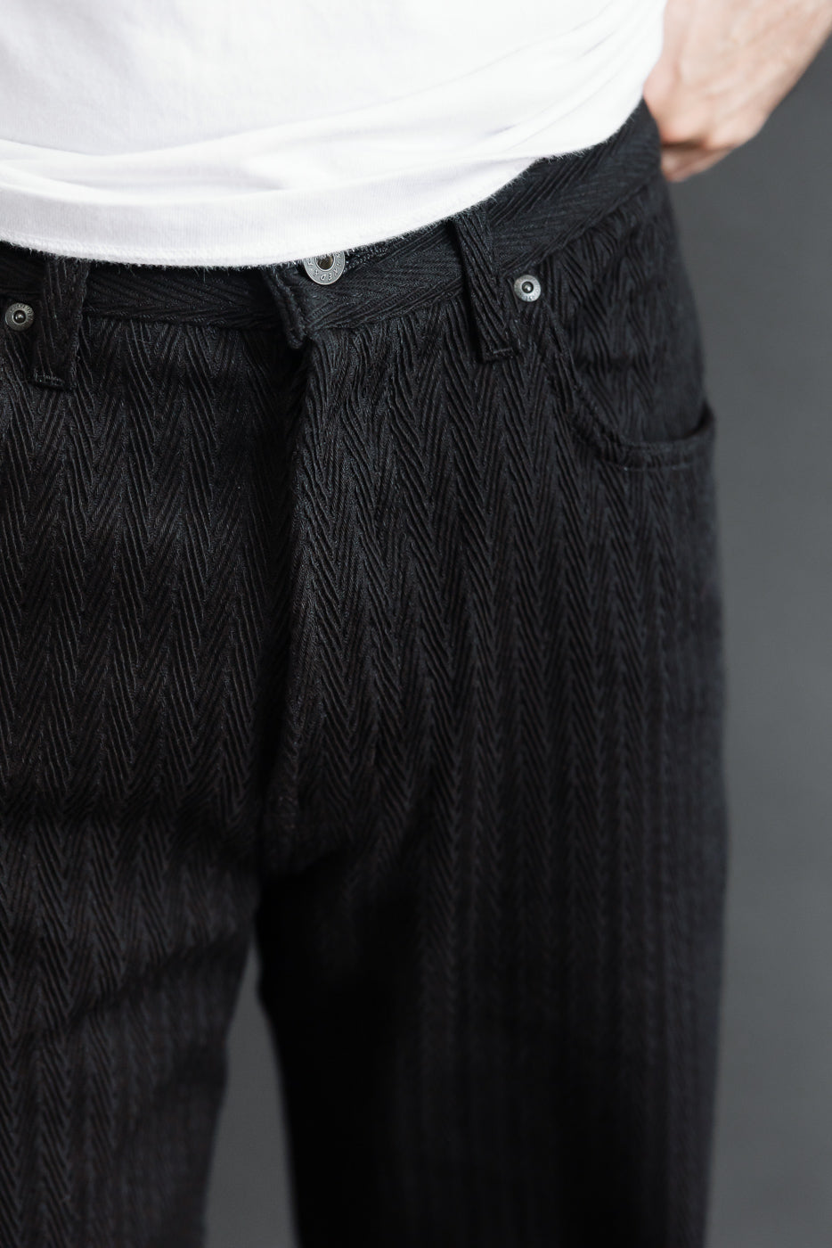 Close-up front view of black herringbone textured trousers on a male model, 5'9