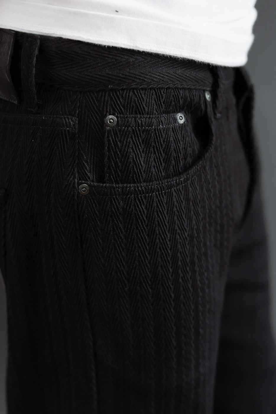 Close-up of the right side pocket and herringbone texture on black textured trousers.