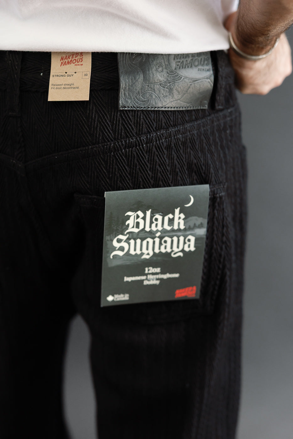 Close-up back view of black herringbone dobby fabric on pants, showing pocket and brand tag.