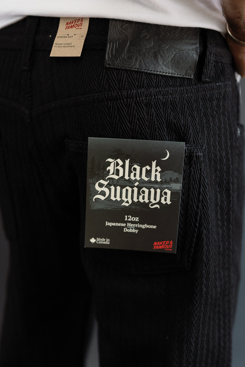 Close-up back view of black Japanese herringbone dobby fabric with leather patch and product tag.