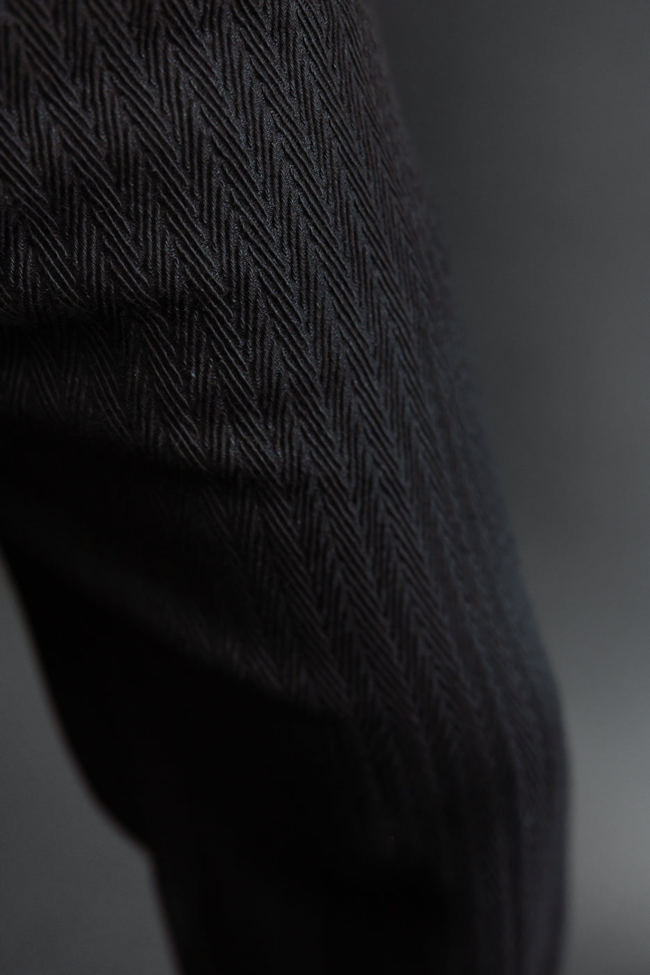 Close-up of the dark charcoal herringbone fabric texture on a garment sleeve.