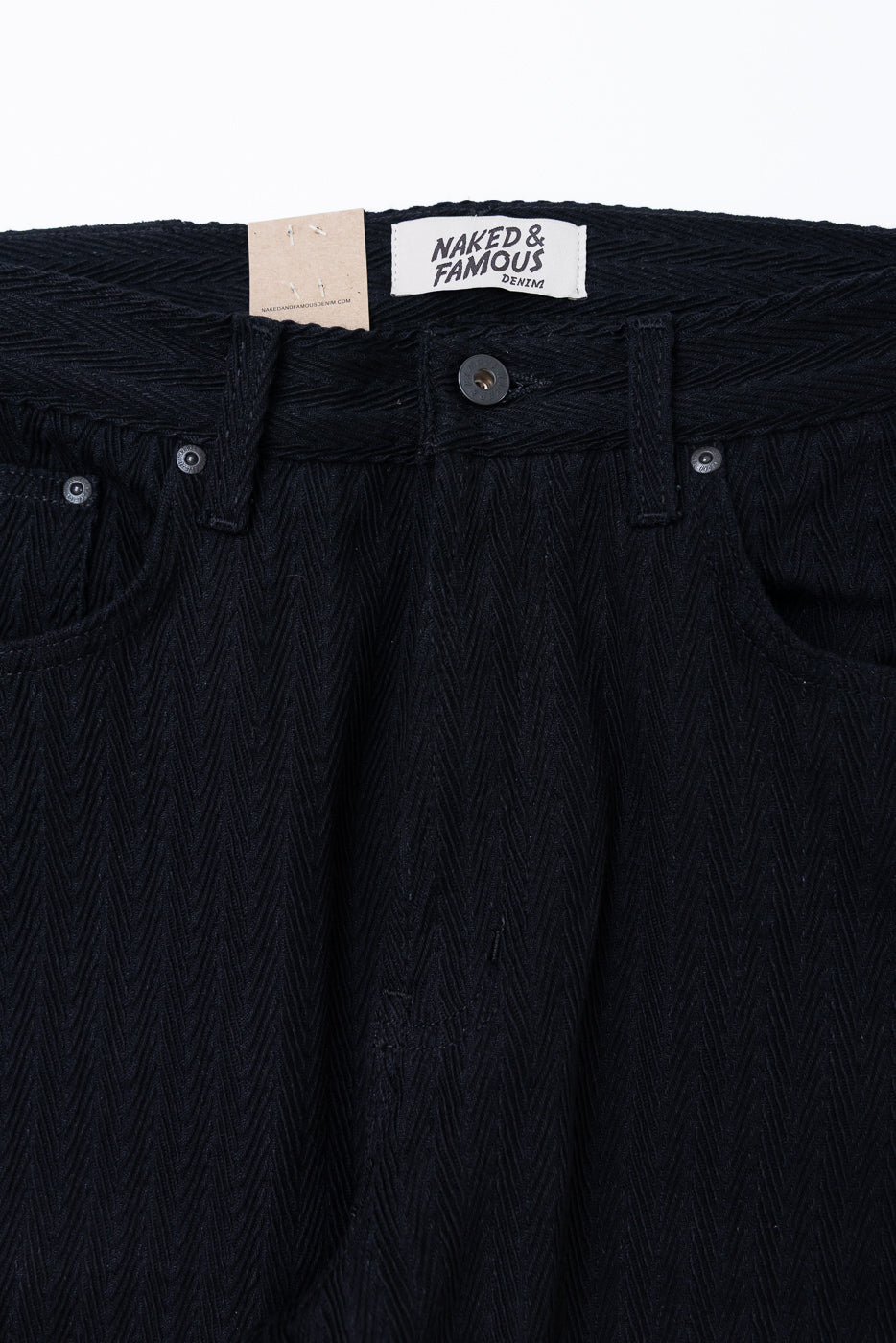 Close-up front view of black herringbone textured trousers showing waistband, button, and tag.