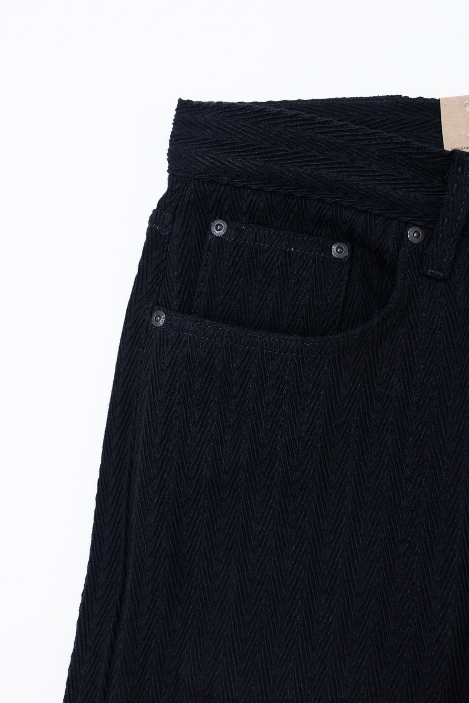 Close-up front view of black herringbone textured trousers showing pocket and waistband detail.