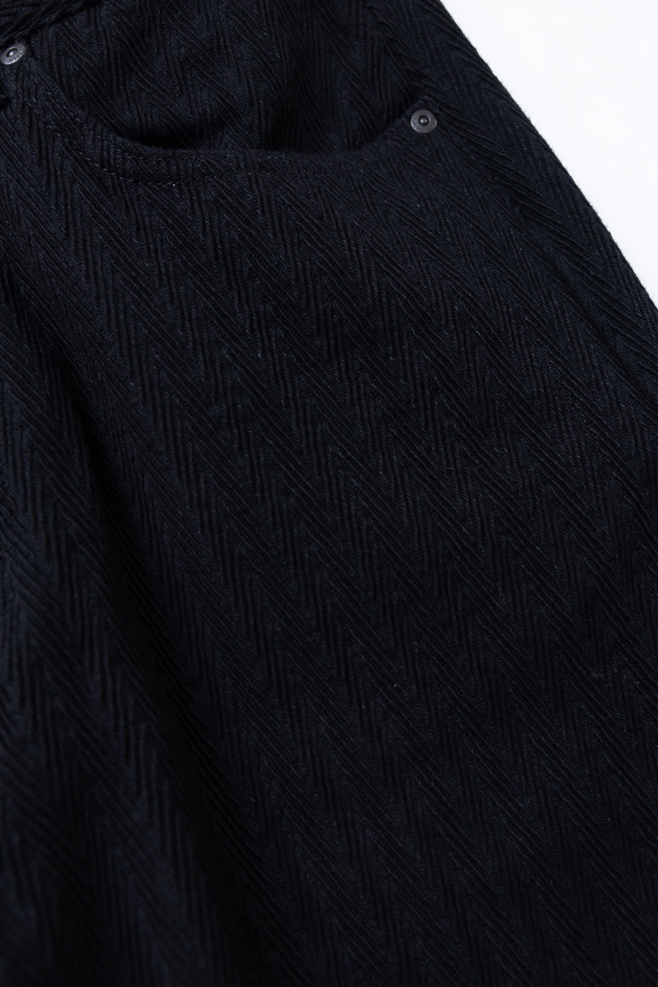 Close-up of the front fabric texture and pocket detail on black herringbone patterned trousers.
