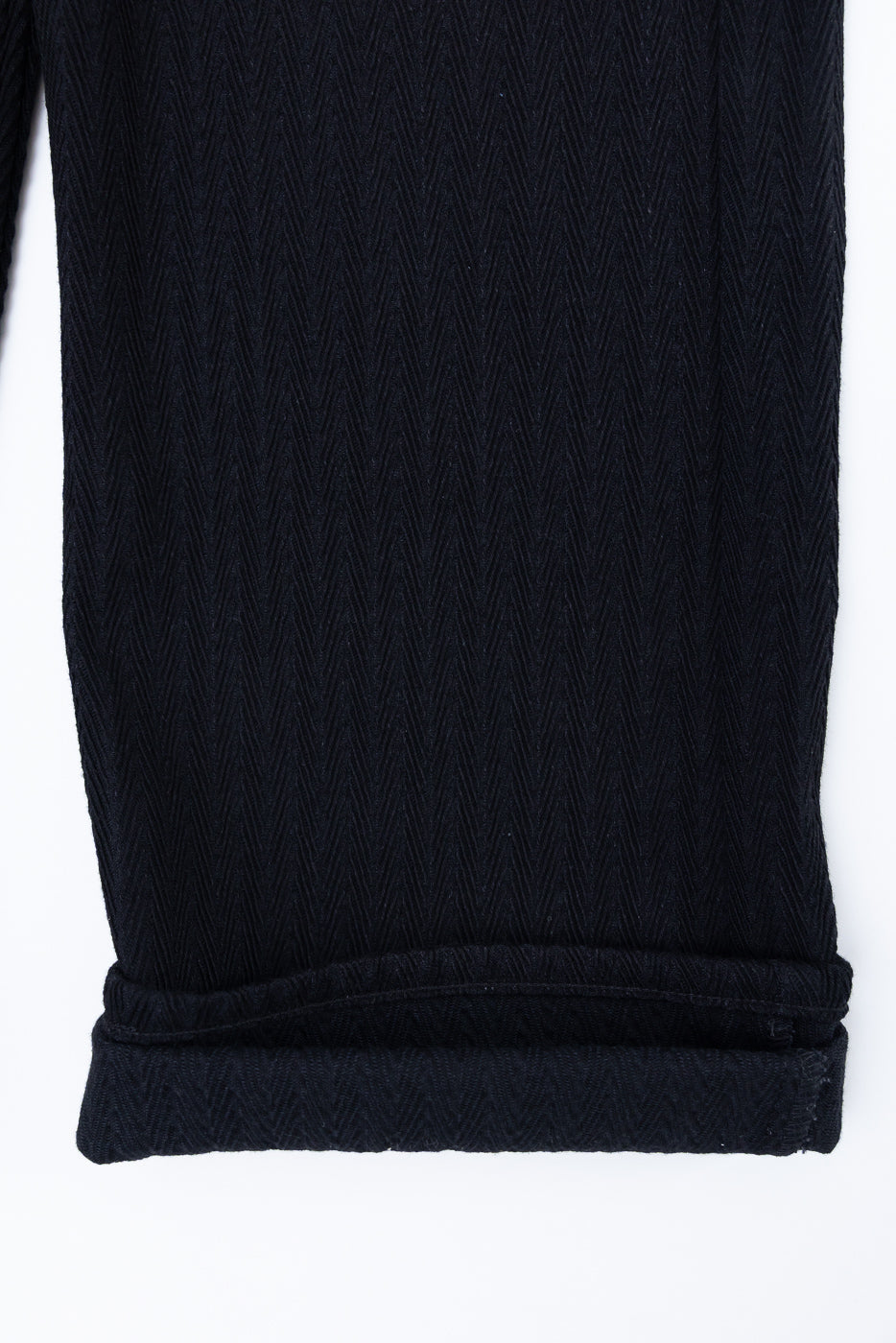Close-up of the bottom hem and cuff detail of black herringbone textured fabric.