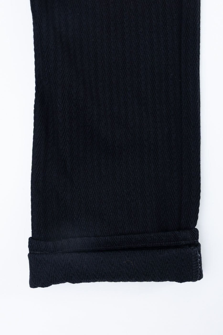 Close-up of the bottom hem and cuff detail of black herringbone texture fabric.