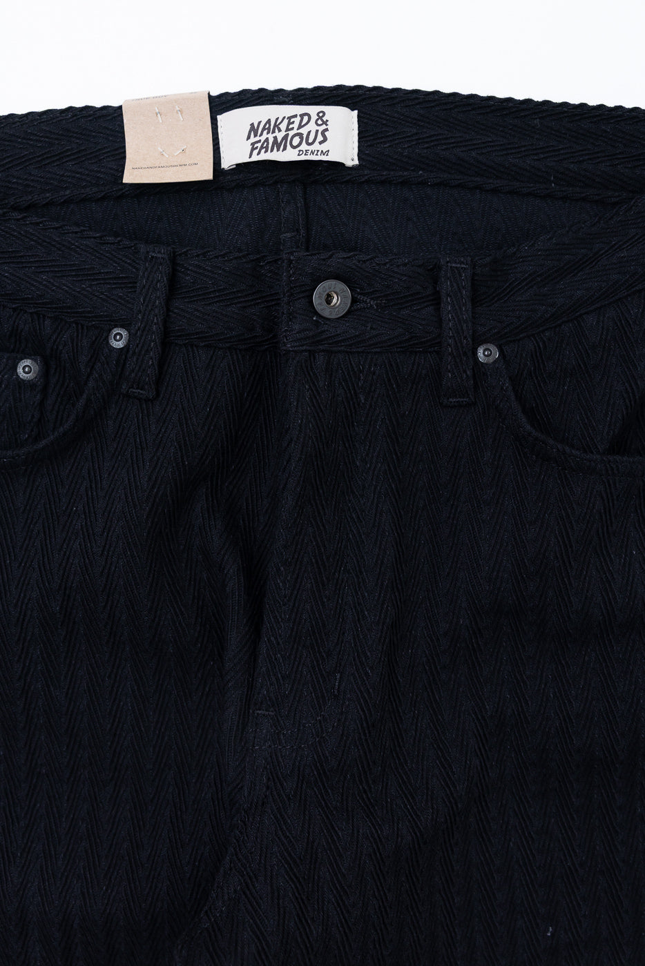 Close-up front view of Naked & Famous denim waist, showing button, belt loops, and fabric texture.