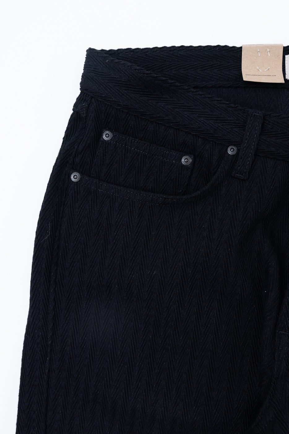 Close-up front view of black herringbone texture fabric on casual trousers showing waistband and pocket.
