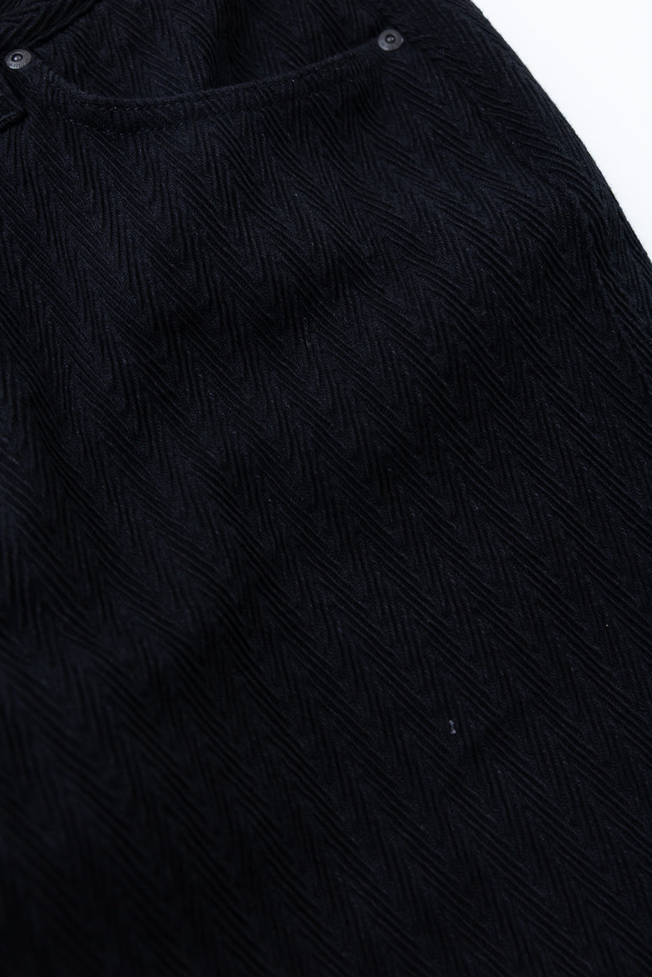 Close-up of the front waistband and textured black fabric of a pair of trousers.
