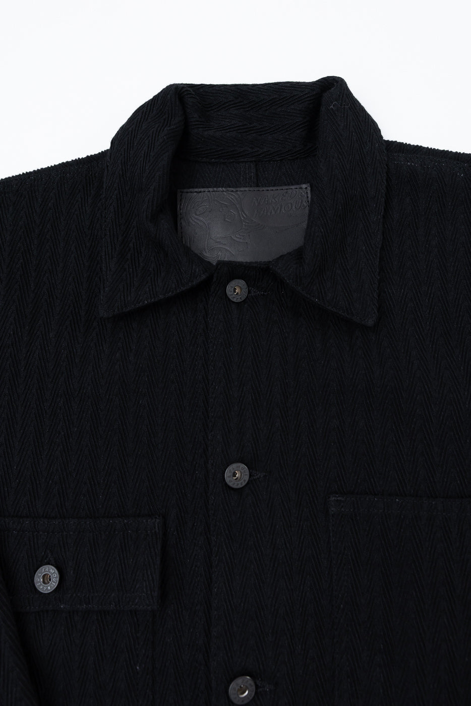 Close-up front view of black textured fabric shirt showing collar, buttons, and chest pocket.