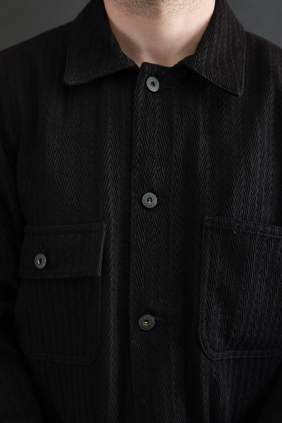 Close-up front view of a black herringbone texture button-up shirt showing collar and chest pockets.