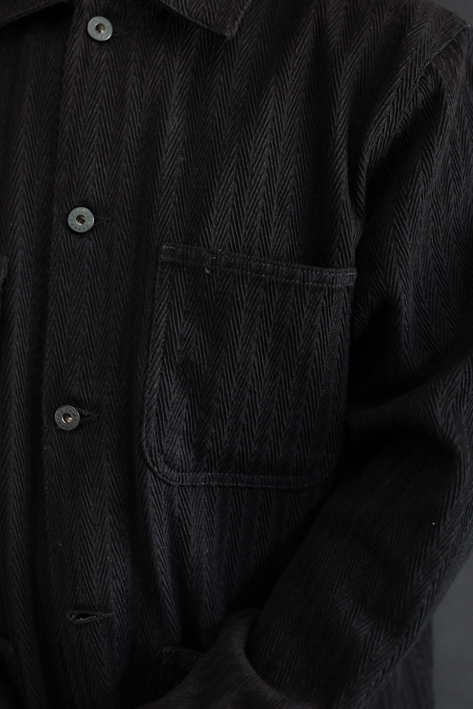 Close-up front view of a black herringbone texture shirt showing the chest pocket and buttons.