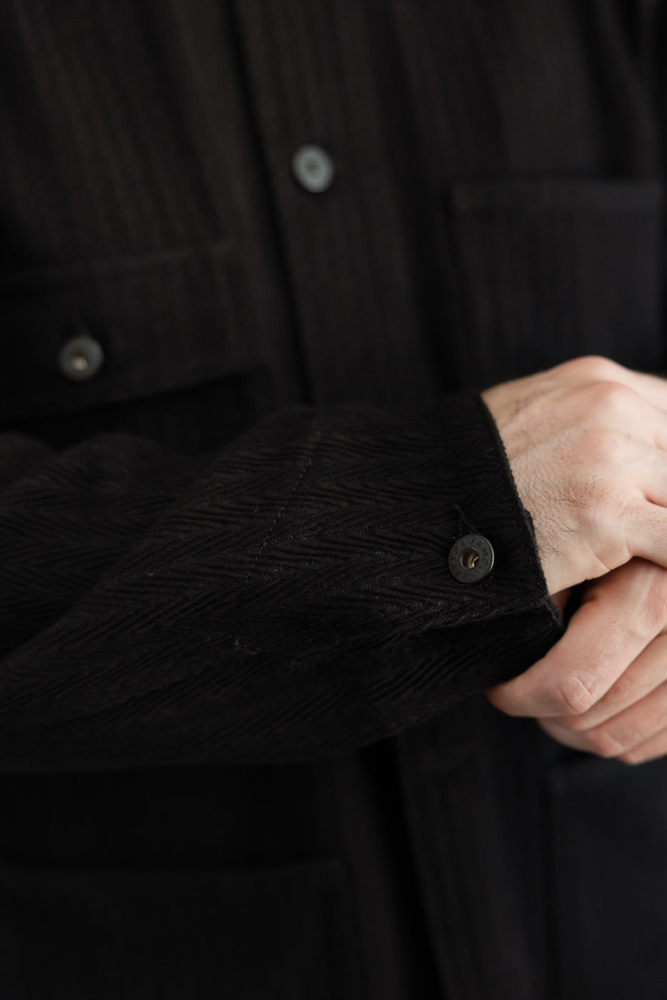 Close-up of the cuff and button detail on a black corduroy shirt sleeve, worn by a male model.