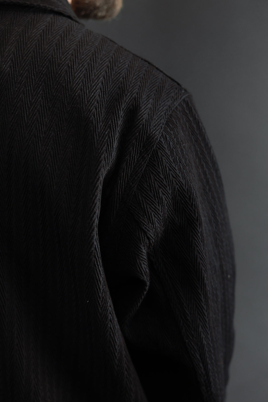 Close-up view of the back and right sleeve showing black herringbone fabric texture.
