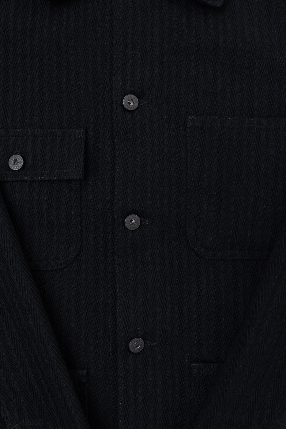 Close-up front view of black herringbone fabric shirt showing button details and chest pockets.
