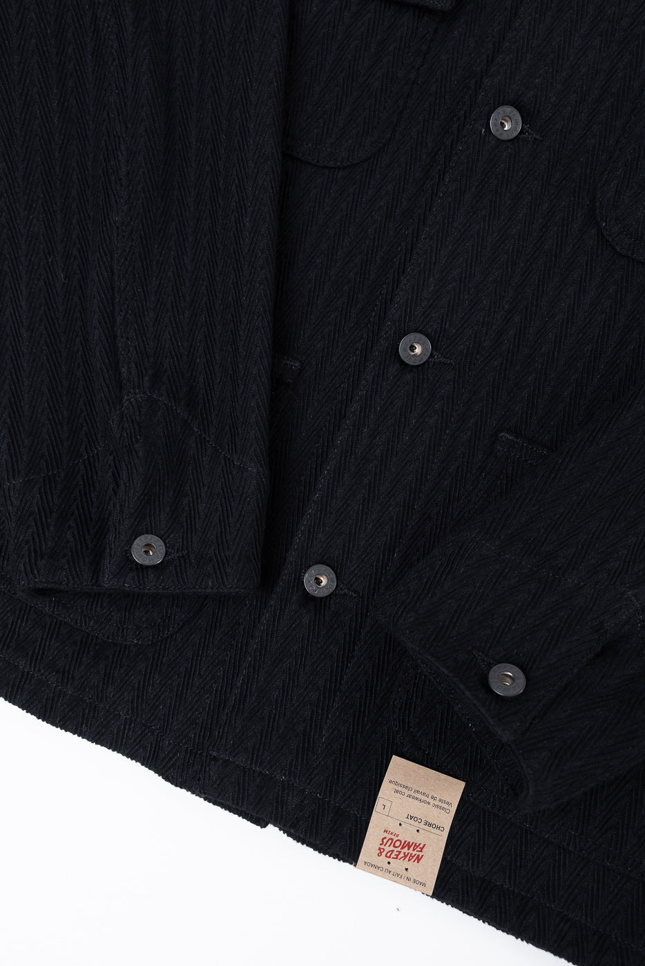 Close-up of the back hem and bottom tag of a black textured chore coat garment.
