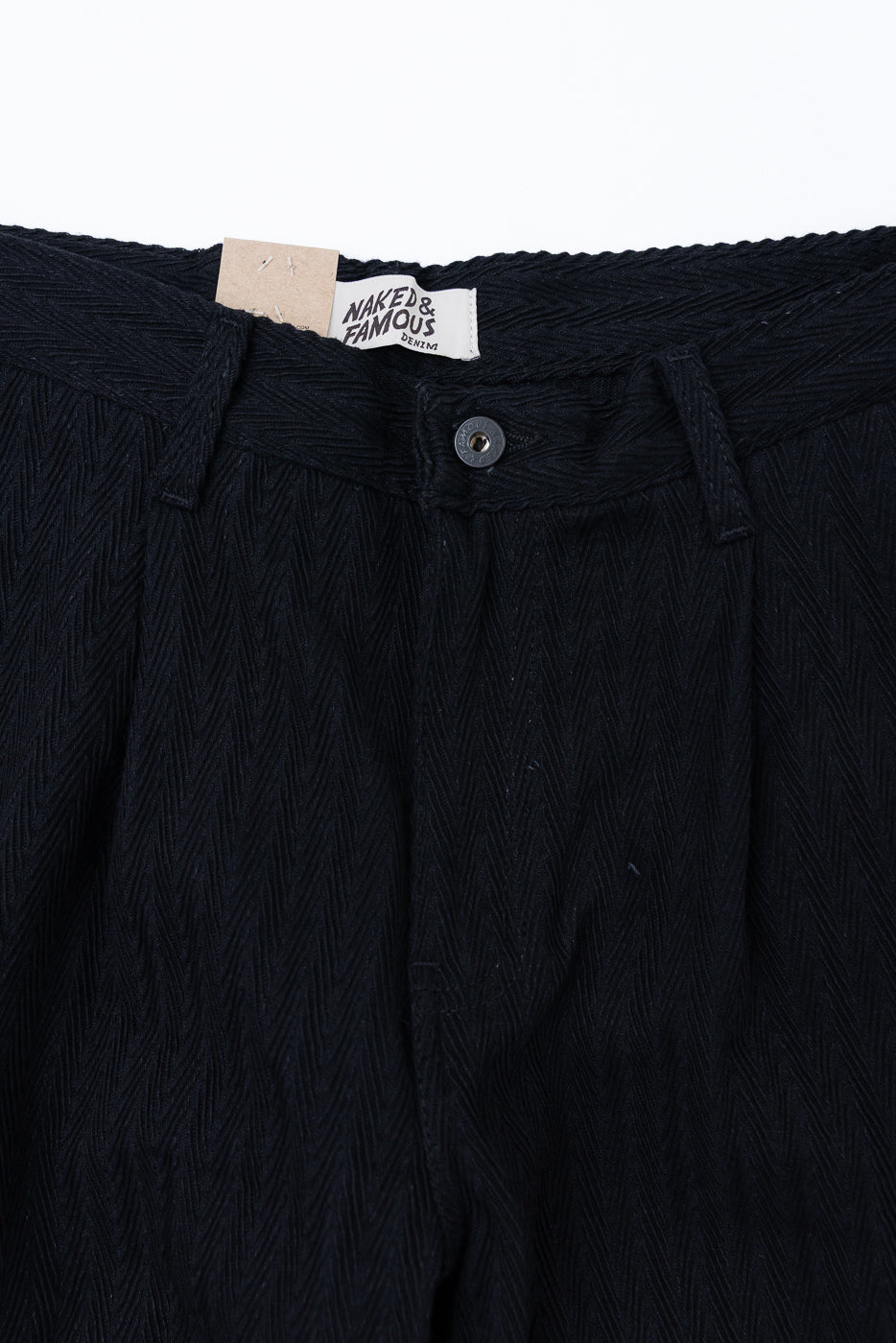 Close-up front view of Naked & Famous denim trousers showing herringbone texture and waist tag.