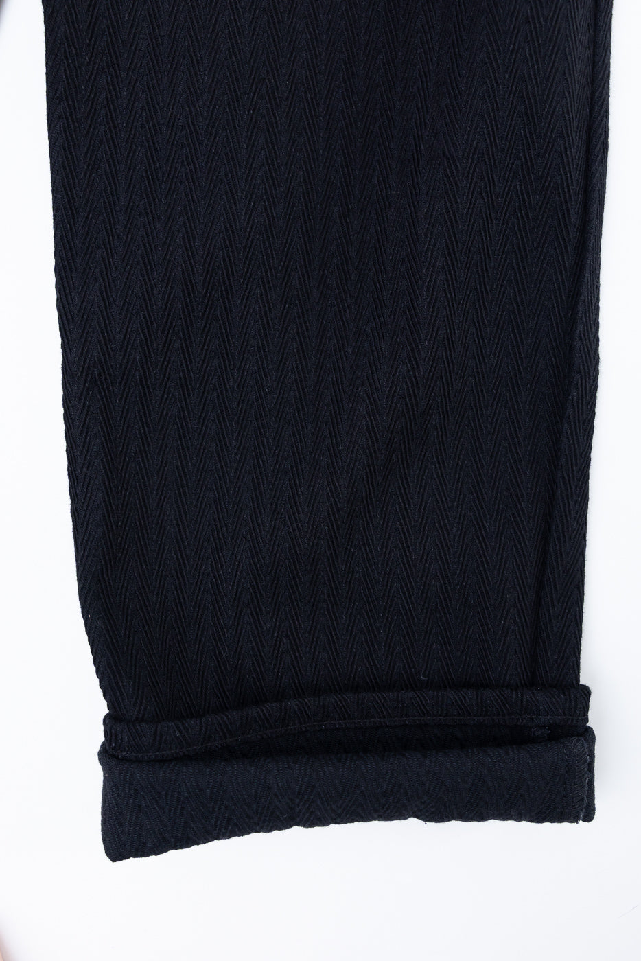 Close-up of the bottom hem and rolled cuff of black herringbone fabric trousers.
