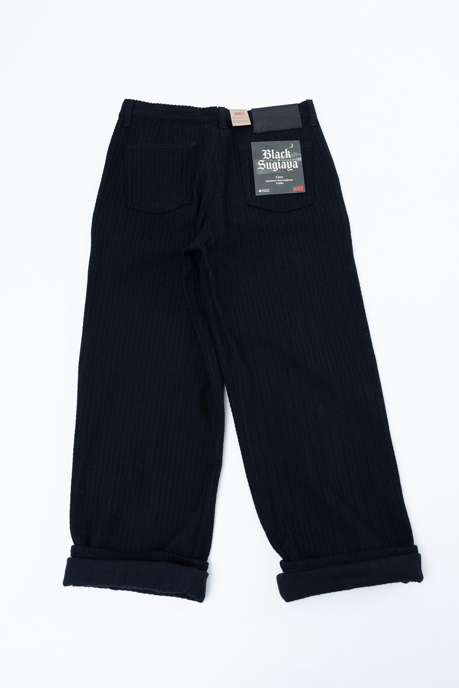 Flat lay, back view of black corduroy trousers showing texture and brand tag.