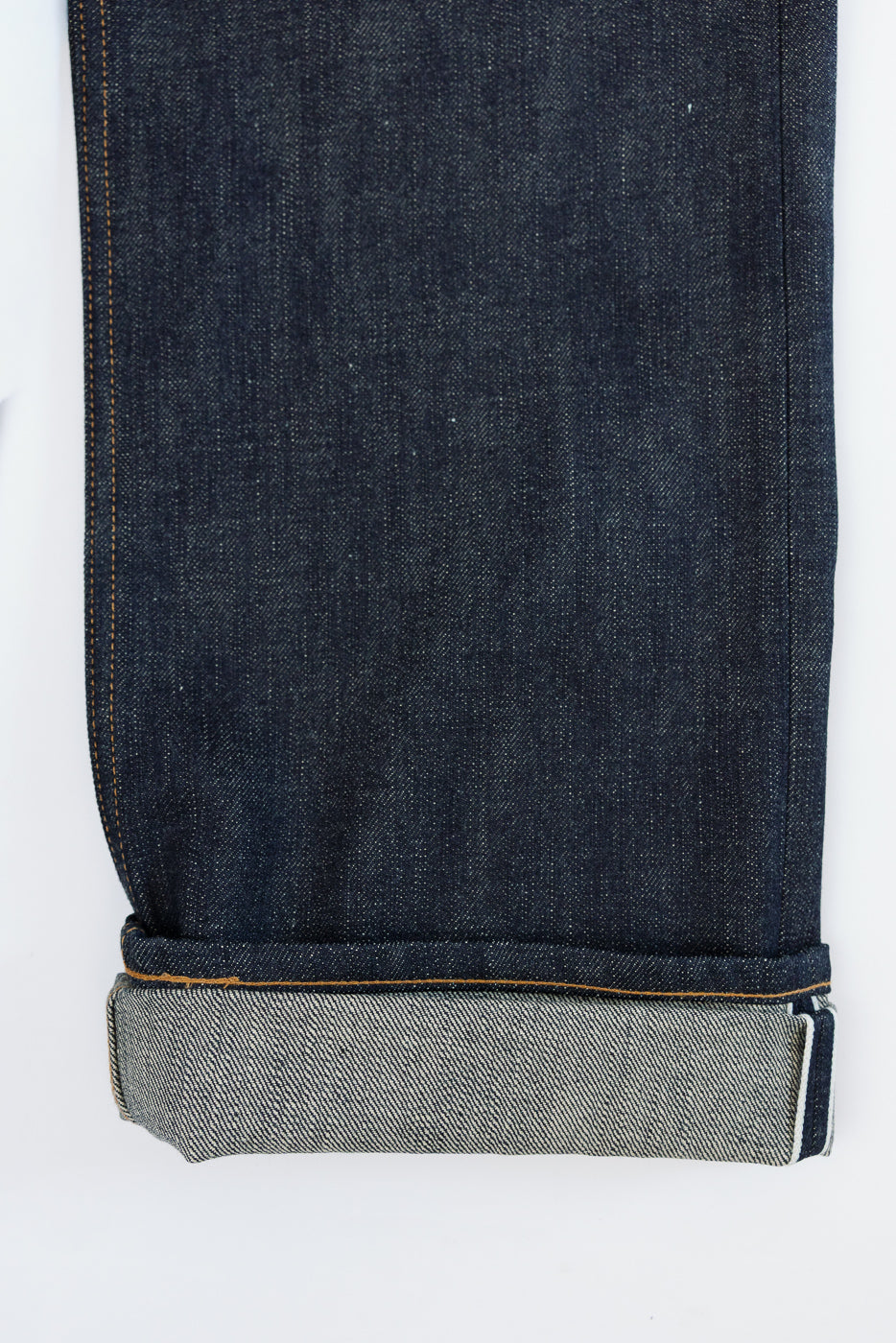 Close-up front view of dark selvedge denim jeans leg, showcasing raw hem, orange stitching, and contrasting inner cuff texture