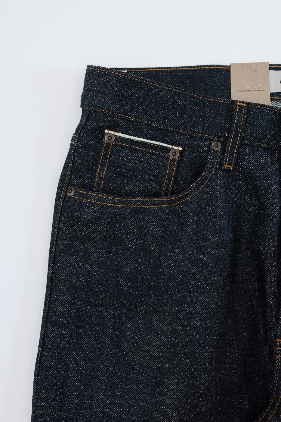 Close-up front view of dark selvedge denim jeans with orange stitching, button fly, and back pocket details