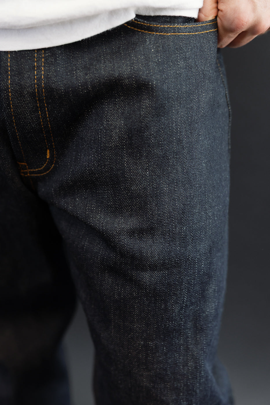Close-up front view of dark selvedge denim jeans with orange stitching, worn by male model.