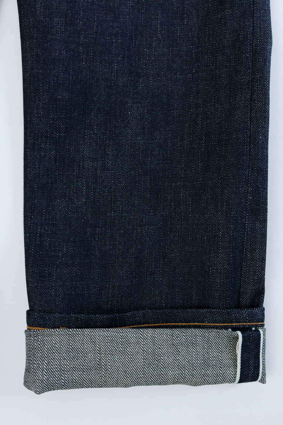 Close-up of selvedge denim jeans hem, showcasing raw edge and fabric texture, front view